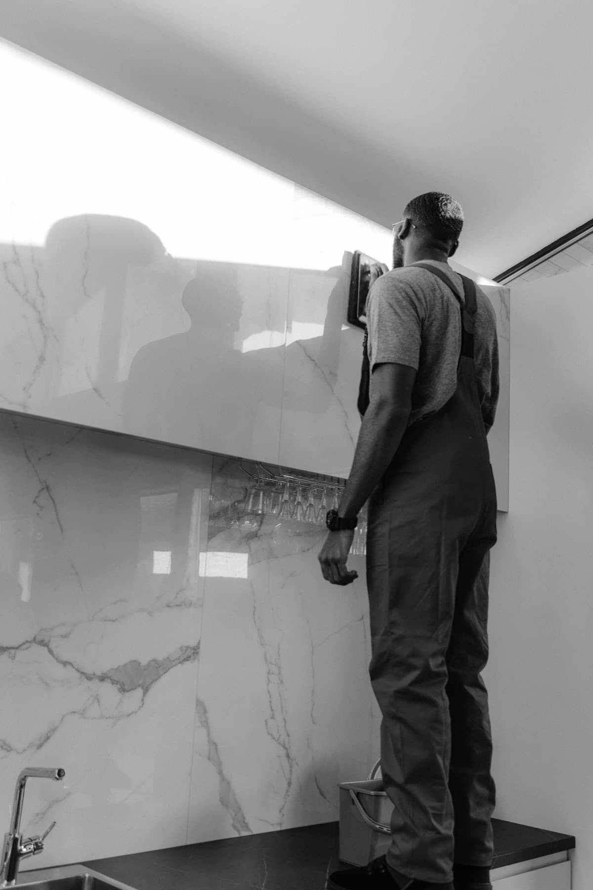 Black and white photograph of a craftsman installing a polished marble backsplash